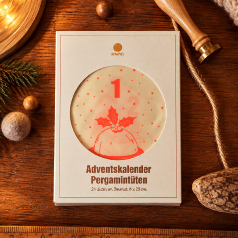 White Advent calendar box on a wooden table; round window shows the number 1 with a red holly design around it. Elements around include pine, string, and a ruler edge in the frame.