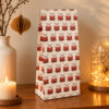 Tall gift box with a red drum pattern sits on a wooden table, flanked by a lit candle and a glass dome with fairy lights.