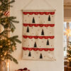 Advent calendar hanging on a light fabric wall, with red semicircular pockets and small Christmas-tree motifs.