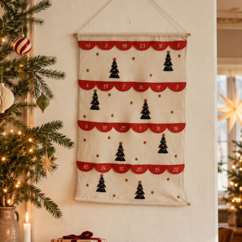 Advent calendar hanging on a light fabric wall, with red semicircular pockets and small Christmas-tree motifs.