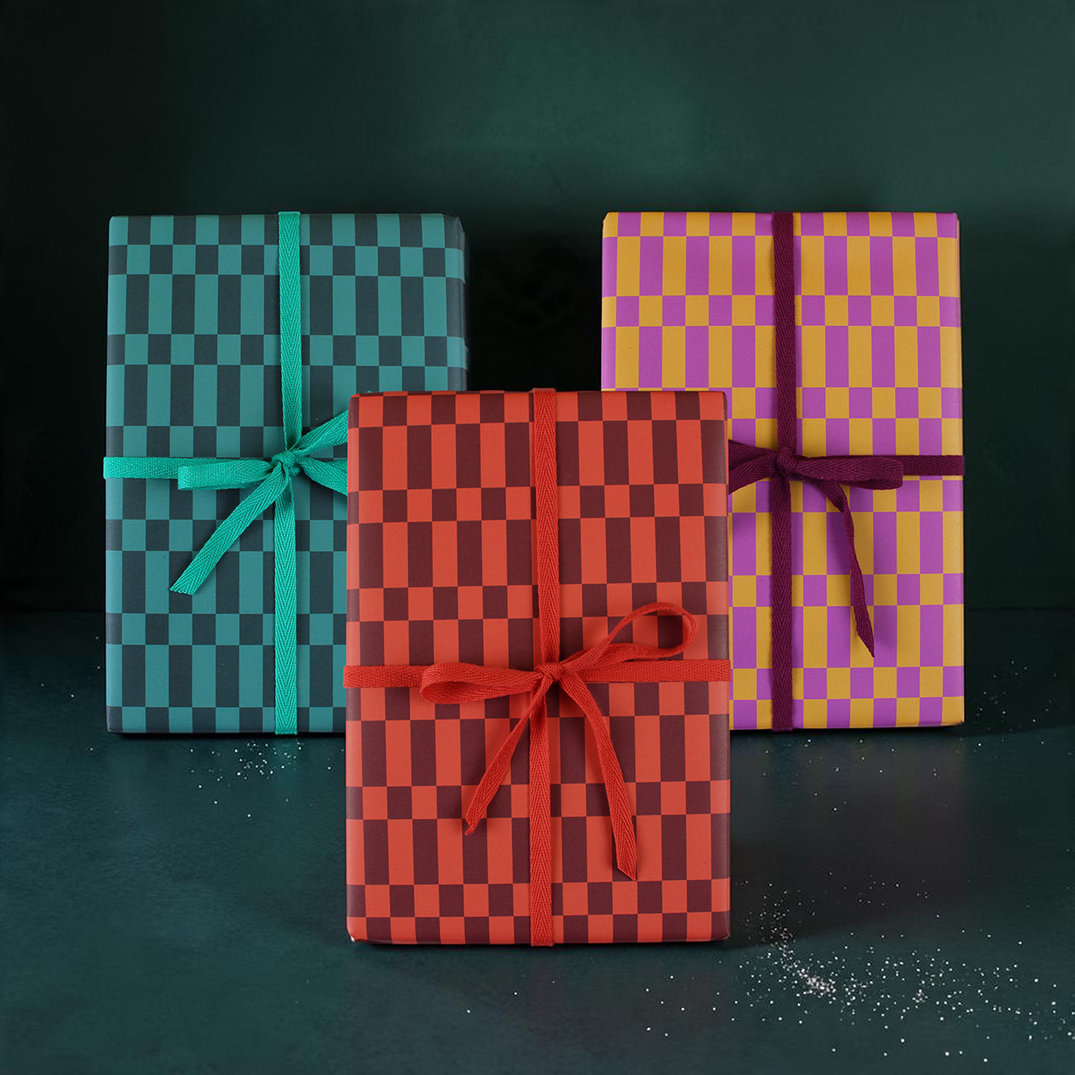 Three colorfully wrapped gift boxes with checkerboard patterns in teal, red, and purple, each with a matching ribbon on a dark background.