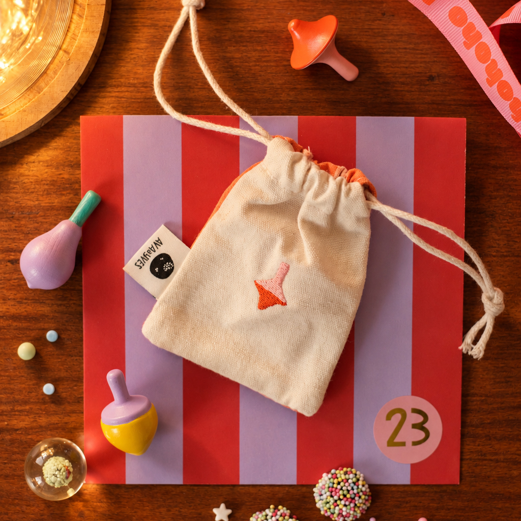 Striped gift box with a drawstring cloth pouch on top, surrounded by small baby toys and candy on a wooden surface.