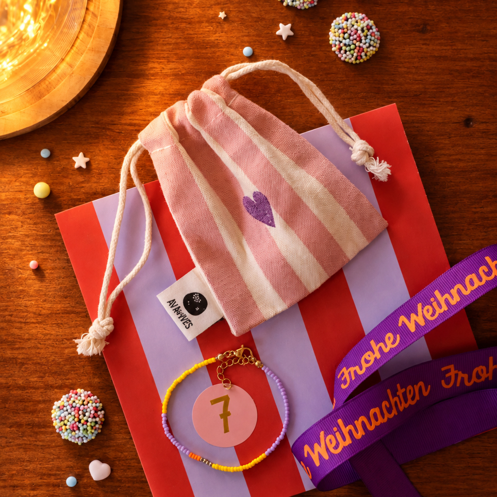 Pink striped drawstring pouch resting on red-and-purple gift bags, with a beaded bracelet marked with the number 7 and a 'Frohe Weihnachten' ribbon nearby.