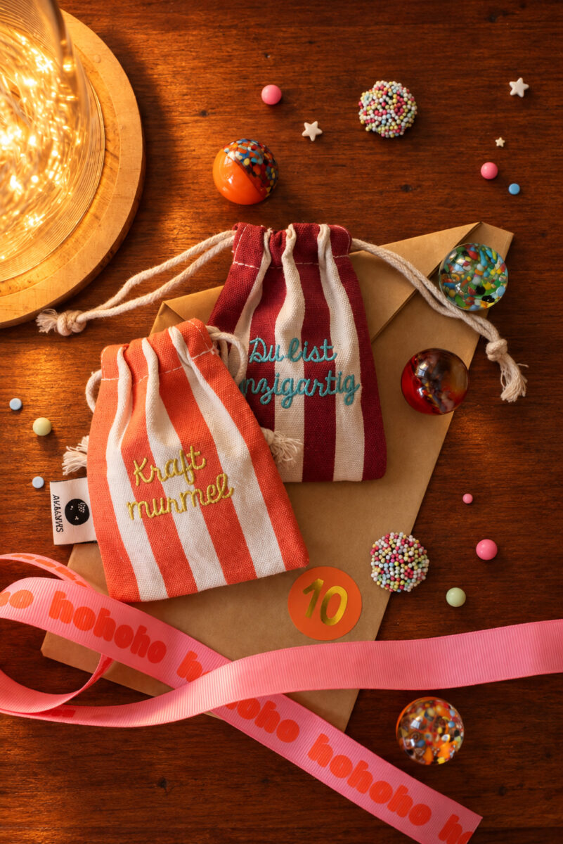 Two striped drawstring gift bags on a wooden table surrounded by candy decorations and a pink ribbon for a festive presentation